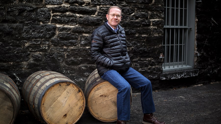 Master Distiller Chris Morris sits on a bourbon barrel in front of a building